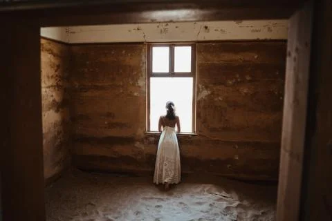 Bride looking through window of old desert house on her wedding day Foto stock