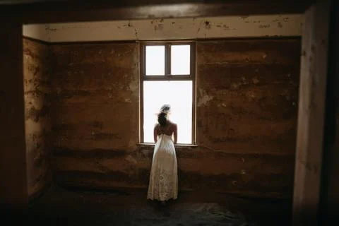 Bride looking through window of old desert house on her wedding day Foto stock