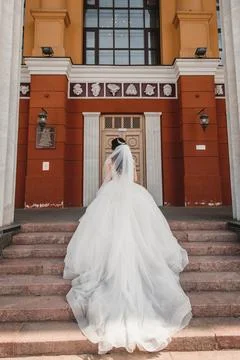 Bride with a lush long train stands with her back on the stairs Stock Photos