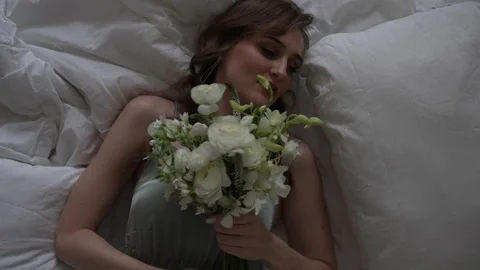 Bride lying in wedding gown on bed with flower bouquet 库存影片 267874880