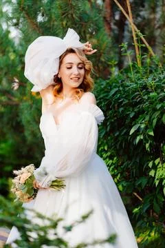A bride in an open-shouldered dress poses against the backdrop of greenery Stock Photos