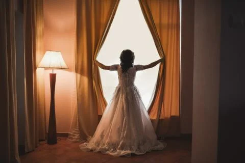The bride opens the curtains on the huge white window. Stock Photos