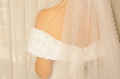 Bride prepares for wedding in long white dress with veil in  bright room with Stock Photos