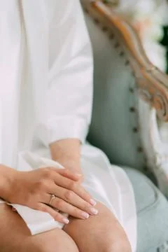 Bride in a robe sits on the bed with her hands clasped, on the finger of the Stock Photos