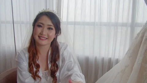 Bride In Robe Sitting By Window With Bridal Gown On Display Video stock 333358626