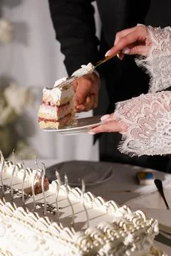 Bride serves a slice of wedding cake on a plate, separated from the large des Stock Photos