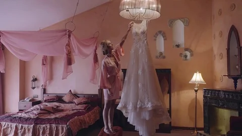 Bride in silk robe takes her dress from the chandelier . Morning preparation Stock Footage 85039894