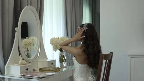 The bride sits in front of the mirror and adjusts the tiara on her head Vidéo 261688147