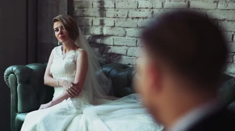Bride sitting on a leather sofa and look at her groom slow motion Stock Footage 54082963