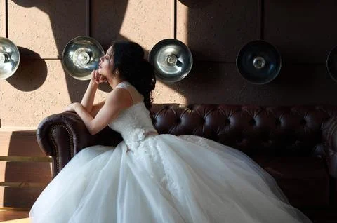 The bride is sitting on the sofa and looking out the window.sun ray.wedding g Stock Photos