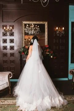 The bride is standing in front of a mirror in a beautiful room. Stock Photos
