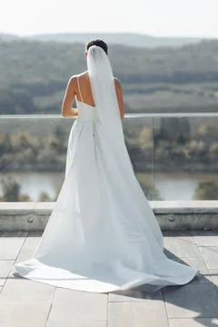 Bride stands backlit on a terrace overlooking hills and water Foto stock