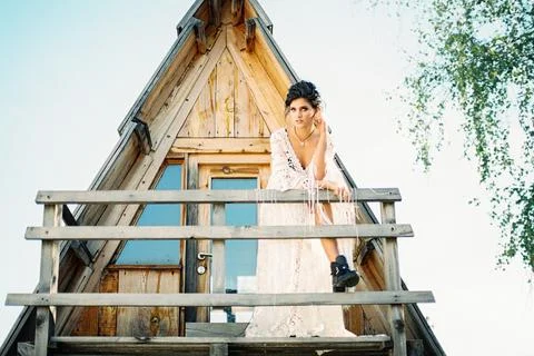 Bride stands on the balcony of a triangular house leaning against a wooden Stock Photos