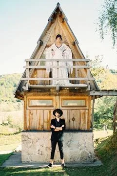 Bride stands on the balcony of a triangular house, above the groom standin... Stock Photos