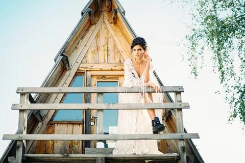 Bride stands on the balcony of a triangular house leaning against a wooden... Stock Photos