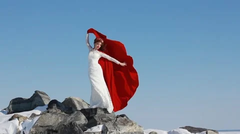 Bride stands on cliff with red flowing fabric Stock Footage 48785666