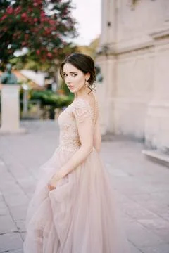Bride stands near an ancient building holding the hem of her dress with her hand Stock Photos