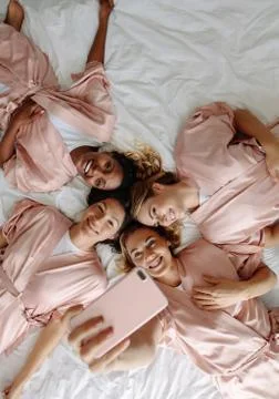Bride taking selfie with bridesmaids while lying on bed Stock-Fotos