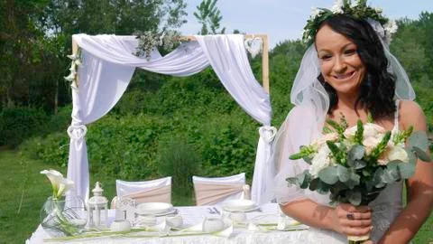 The bride with a veil in front of the wedding table holds a bouquet with a happy Foto stock