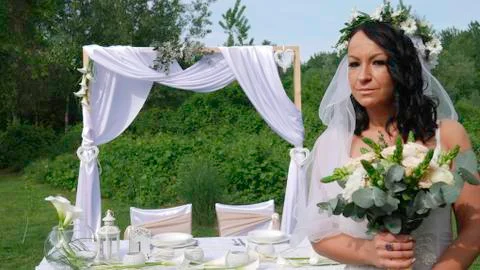 The bride with a veil in front of the wedding table holds a bouquet. Stock Photos
