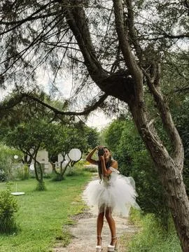 Bride walking beneath a spreading garden tree in a white tulle dress Stock Photos