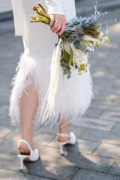 A bride walks gracefully on a cobblestone path, holding a vibrant bouquet of  Stock Photos