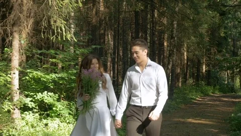 The bride in a white dress and her fianc are strolling through the forest. Stock Footage