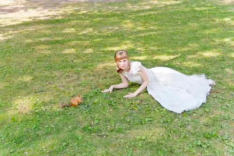 Bride in white lying on grass next to the squirrel Foto stock