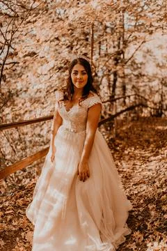 Bride in white wedding dress walks through autumn forest on fallen orange lea Stock Photos