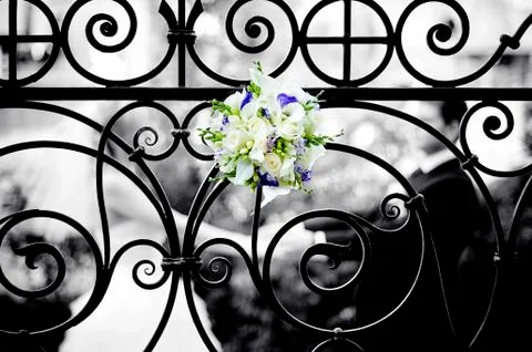 A bride's bouquet is inserted into an elegant forged fence, behind which the Stock Photos