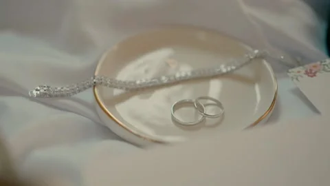 The bride's bracelet and rings in a ceramic saucer with bridal shoes next to it Stock Footage 221510183
