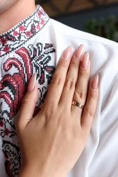 A brides delicate hand with a wedding ring rests on the grooms chest, both dr Stock Photos