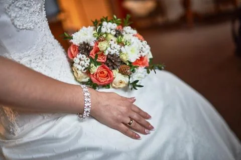 Bride's hand with wedding ring resting on lace dress holding vibrant floral.. Stock Photos