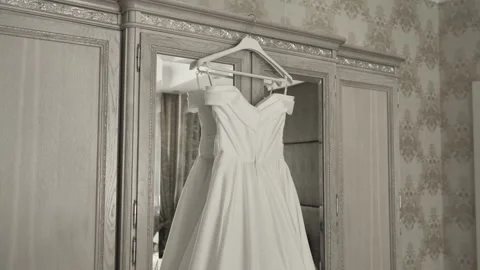 The bride's white dress hangs on a rack in the bright bedroom Stock Footage 213633316