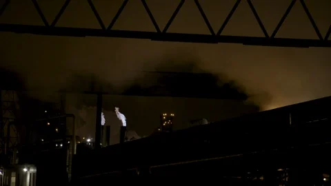 Bridge and warehouse silhouetted against night sky with fire stack in background Stock Footage 89945397