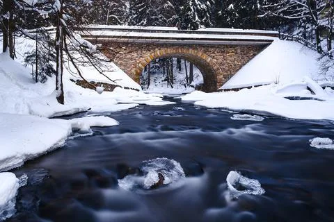 Bridge over river in winter, surrounded by forest and snow Stock Photos