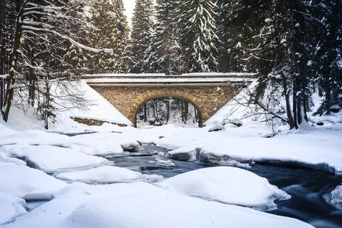 Bridge over river in winter, surrounded by forest and snow Stock Photos