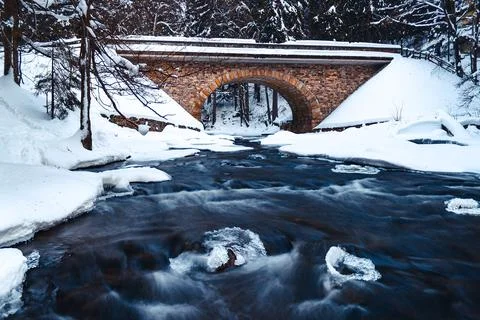 Bridge over river in winter, surrounded by forest and snow Stock Photos
