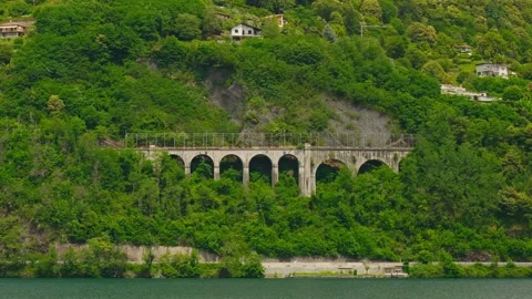 Bridge with Rounded Concrete Pillars Against Lush Green Cliff at lake 库存影片 340911142