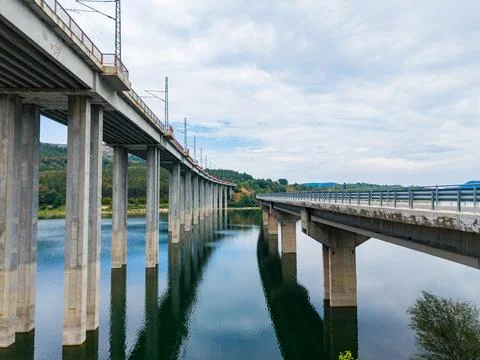 Bridge spanning across water under cloudy sky in rural area with reflection.. Foto stock