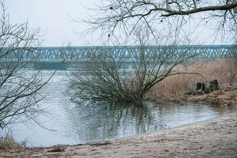 A bridge spanning a tranquil lake with a tree in the foreground Foto stock