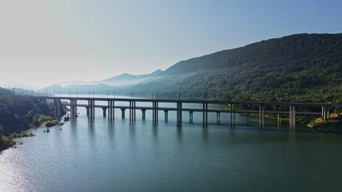 Bridge spans calm waters under a clear sky in a mountainous area Stock Footage 340381988