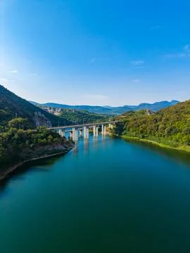 A bridge spans over a river with clear water reflecting the blue sky. Green h Stock-Fotos