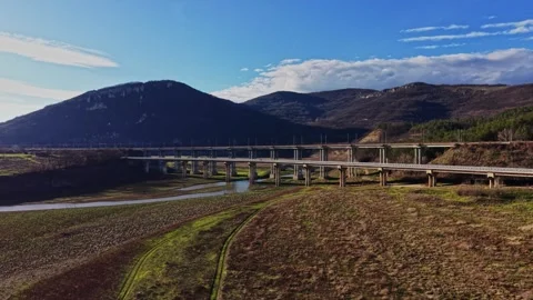Bridge spans river in mountainous region under blue sky and clouds Stockbeeldmateriaal 336547260