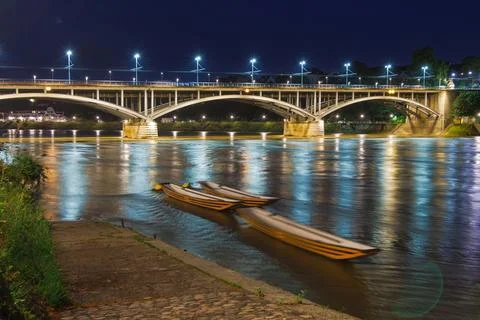 A bridge spans a river at night, with lights illuminating the water Stock Photos