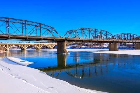 A bridge spans a river with a snowy bank Stock Photos