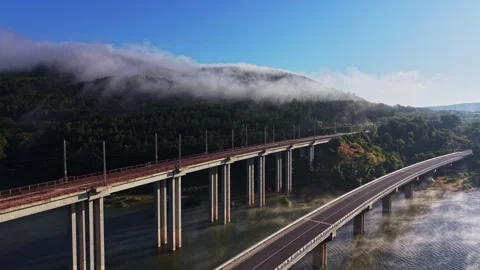 Bridge spans river under morning fog with green hills in the background Stock Footage 339648355