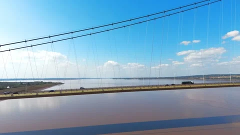 Bridge spans wide river under clear sky. Strings stretch taut against blue 库存影片 343696655