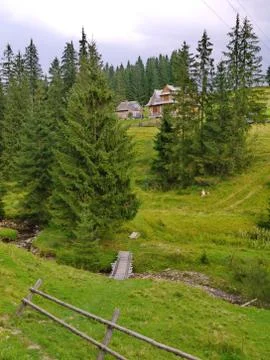 A bridge from a tree through a mountain stream to distant houses on a slope Stock Photos