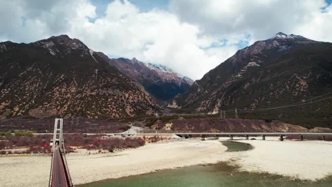Bridges over pale river sediment below rugged Tibetan mountains Vidéo 345884021